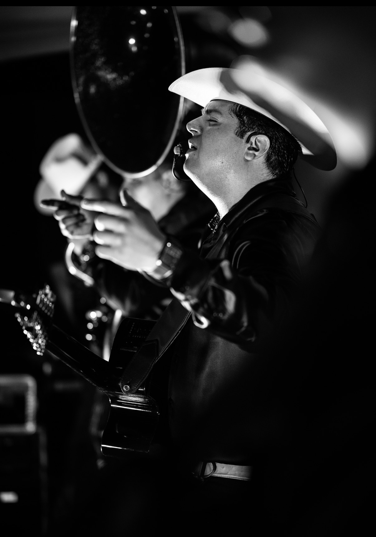 Black-and-white photo of a Regional Mexican singer in a white cowboy hat performing with a guitar